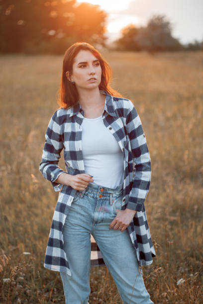 Beautiful brown haired young woman in plaid shirt posing outdoors at sunset.