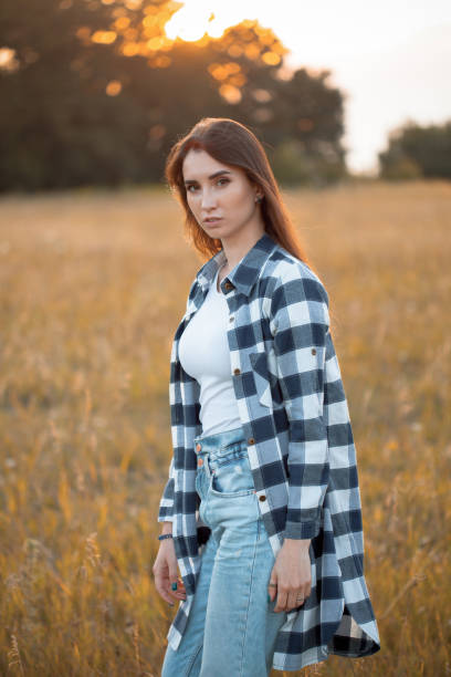 Attractive girl in plaid shirt walking on the field at sunset