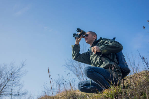 istock A young and handsome man with a large backpack on his back stands atop a mountain, gazing through binoculars at the distant horizons. He enjoys exploring the untouched nature, savoring every moment of his travel adventure 2197498231