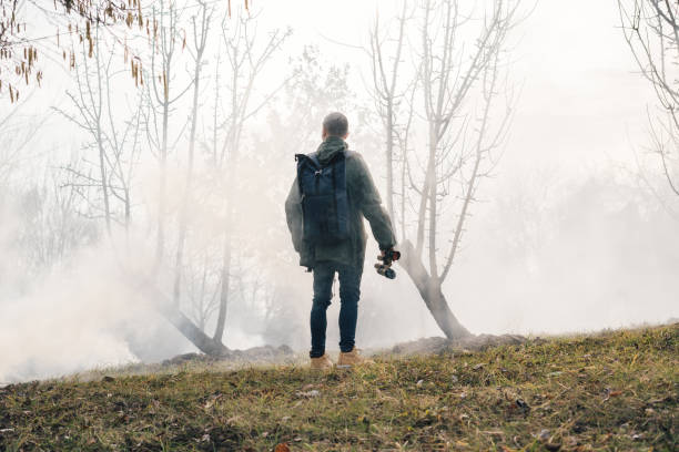 A young man with a large hiking backpack walks through the morning mist, holding binoculars in his hand, enjoying the silence of nature and the magic of adventure.