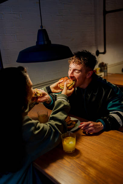 istock Young couple feeding each other burgers in cozy restaurant setting 2197501578