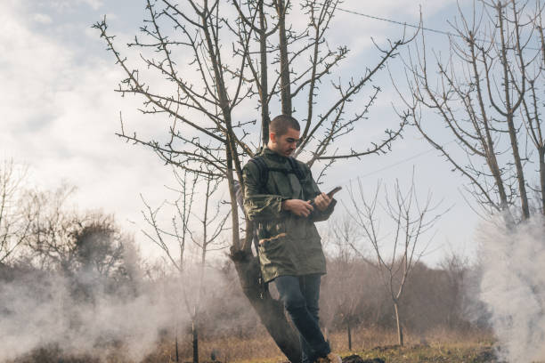 A man is wearing a cowboy hat and a loso in the field. American farmer in a field wearing a jeans hat and with a lasso in the smoke of a fire. A man walks through a burning field in a hat