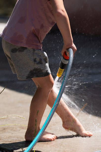 A joyful young girl sprays herself with water from a garden hose, laughing as droplets splash around on a warm summer day.