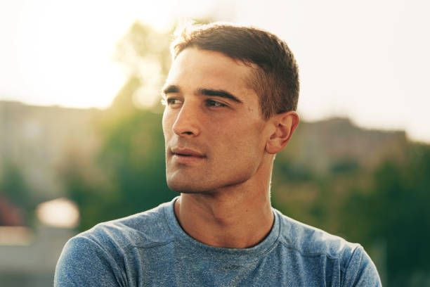 Young man in a blue shirt looking thoughtfully outdoors during golden hour