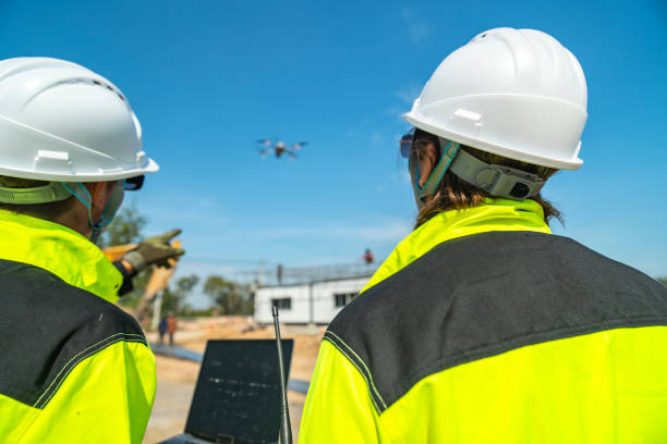 istock Two engineers in high visibility jackets and helmets observing a drone flying over a construction site, with machinery and modular buildings, highlighting technology and site monitoring. 2197510256