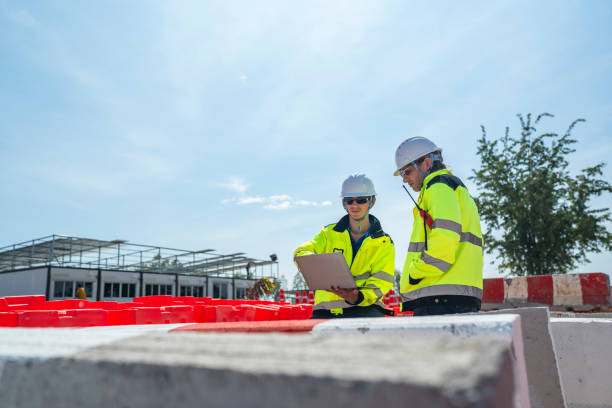 istock Two engineers wearing high visibility jackets discuss construction progress near concrete barricades on-site. One holds a laptop, symbolizing modern planning and collaboration in civil engineering. 2197513937