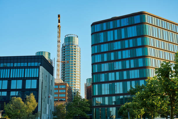 istock Modern glass buildings with construction crane and green trees 2197523684