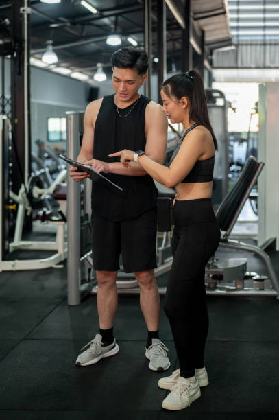 istock Athletic Asian male fitness instructor is discussing and adjusting a workout program with a client 2197525193