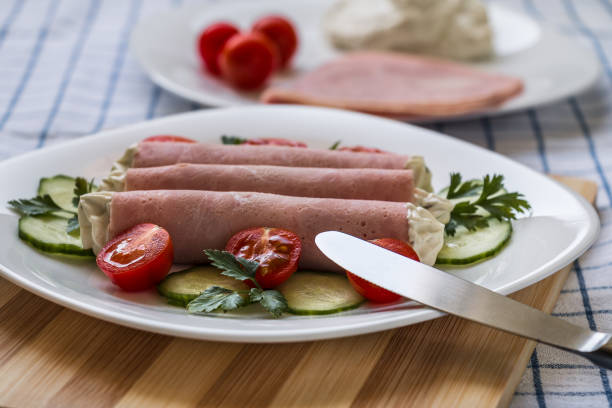 Horseradish ham rolls on a white plate decorated with cucumber tomatoes and parsley leaves.