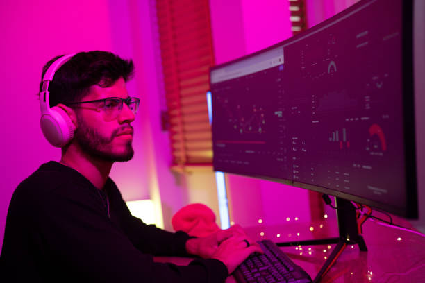 istock Young man working on dual monitors in a modern workspace with purple lighting during the evening 2197537297
