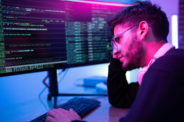 istock Person coding at night in a dimly lit workspace with colorful lighting and computer screens displaying lines of code 2197537337