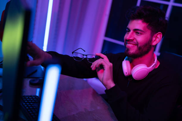 istock Young man enjoying gaming session at home with neon lighting and headset while smiling and holding glasses 2197537391
