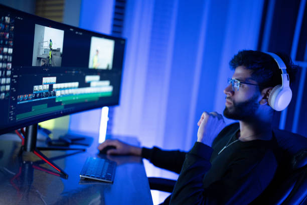 istock Young man engaged in video editing at a computer with multiple monitors in a dimly lit room 2197537448