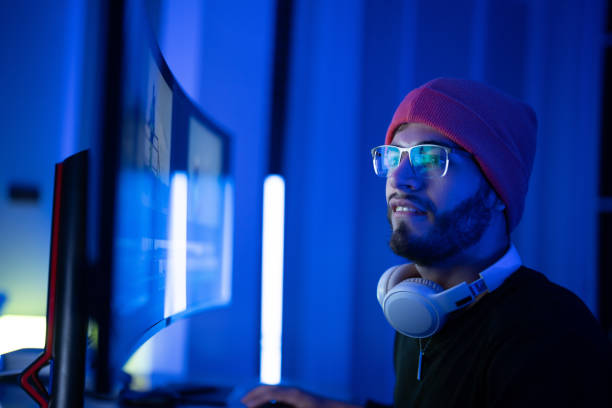 istock Young man gaming in a dimly lit room with neon lighting and modern computer setup 2197537555