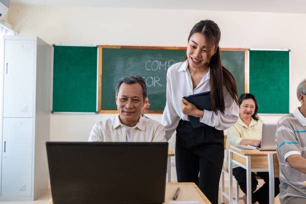 istock Asian female instructor teaching mature students in classroom at school. Attractive teacher motivate and explain senior learner how to use laptop computer during adult education course in tutor class. 2197537835