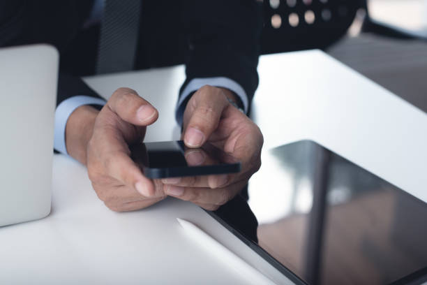 istock Businessman in black suit using mobile phone during working at office with digital tablet and laptop computer on table, close up. Business man surfing the internet at workplace 2197539663