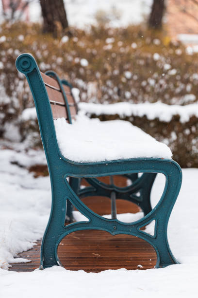 The park bench is covered with snow. It’s a view from the side.