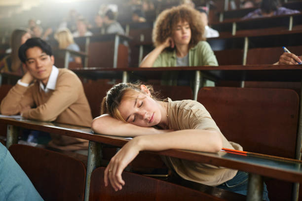 Tired female student fell asleep on a class at lecture hall. Female college student taking a nap during a lecture in amphitheater. male college student sleeping through lecture stock pictures, royalty-free photos & images