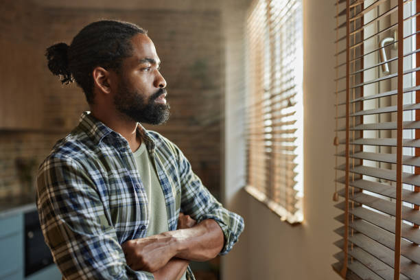 Black man looking through the window at home.