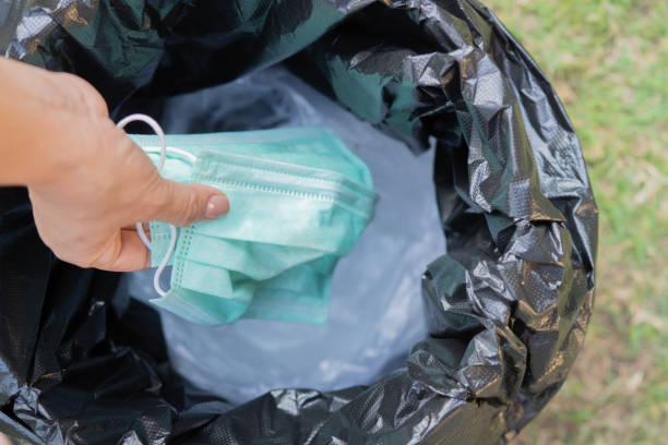 istock Woman's hand throwing Medical face mask into trash. Top view, selective focus. 2197547134