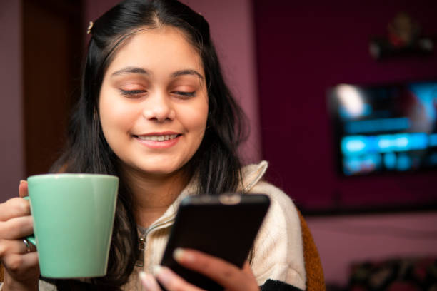 istock Relaxed young woman sitting comfortably in bed with cozy blanket and using a smartphone while drinking a hot cup of coffee in winters and enjoying her leisure time at home. 2197547881