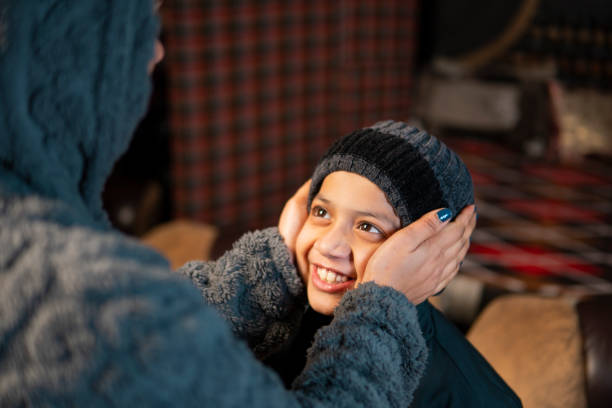 Caring Indian mother putting warm cap on son’s head and getting ready for winter activities.