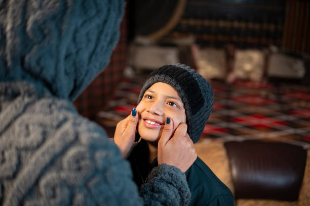 Caring Indian mother pulling her son’s cheeks after putting warm cap on his head and getting ready for winter activities.
