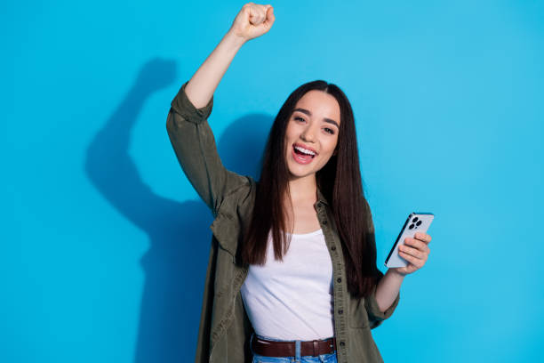 istock Smiling young woman with phone, posing in front of blue background, cheerful expression 2197555167
