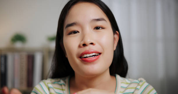 istock Smiling Asian woman using wireless microphone and talking to camera with positive emotion in living room at home. 2197556049