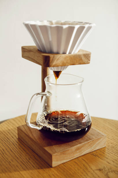 Alternative Coffee Brewing Method With Funnel and Paper Filter Pouring Into Glass Pot on Wooden Table against White Wall