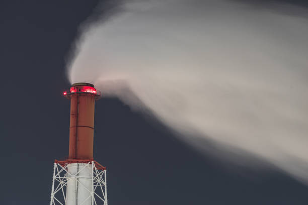 An evocative scene of industrial chimneys releasing smoke during dusk, with warm and cool tones blending in the sky. This image portrays the intersection of human activity and the natural world in the quiet moments before nightfall.