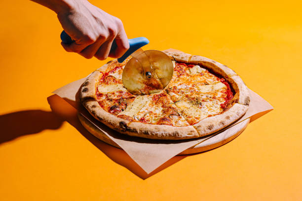 istock Hand slicing a fresh pizza with a pizza cutter on a vibrant yellow background 2197562881