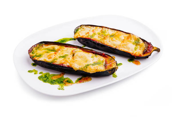 Stuffed eggplants filled with melted cheese sit on a white plate, garnished with vibrant green sauce. This dish showcases a delightful combination of flavors and textures.