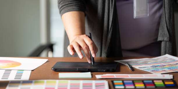 istock Graphic designer using a digital tablet to create designs at a wooden workspace. 2197564625