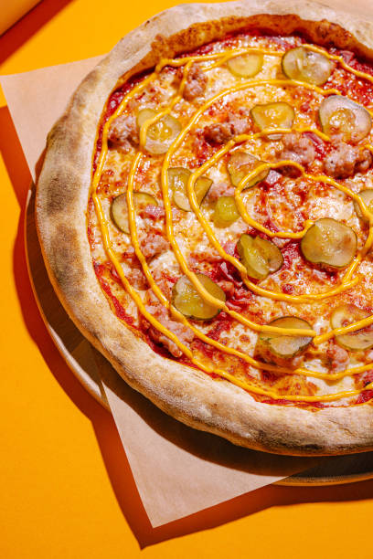 istock Delicious pizza topped with pickles and drizzle, served on a bright yellow background 2197567148