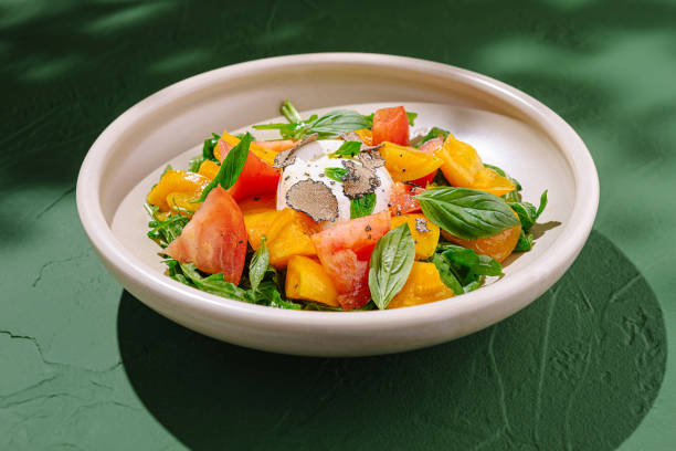 Fresh salad with ripe tomatoes, creamy cheese, and fragrant herbs on a green background