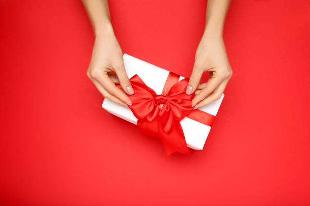 istock Gift box with ribbon and female hands on red background 2197567534