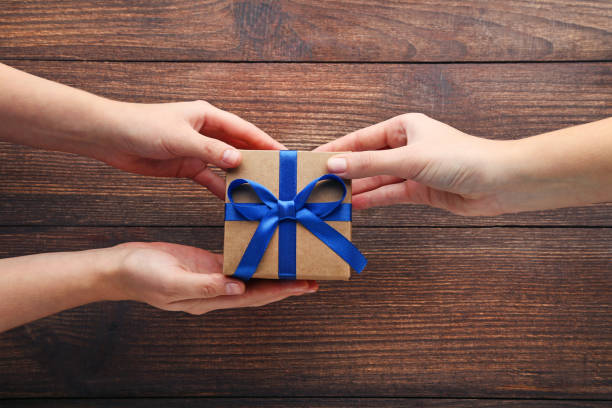 istock Female hands holding gift box with ribbon on wooden table 2197568465