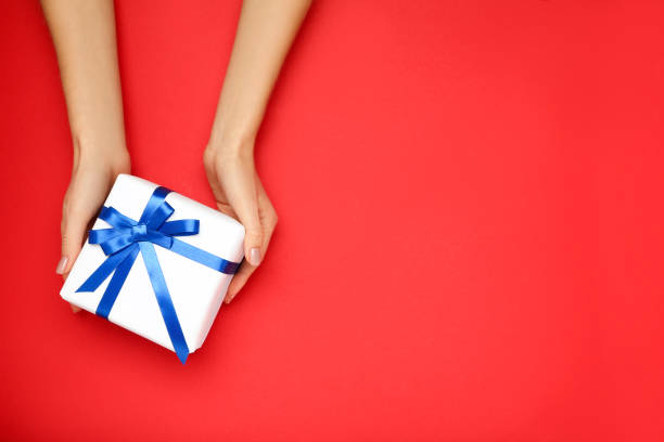 istock Gift box with ribbon in female hands on red background 2197568594