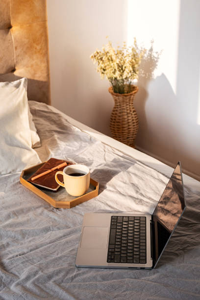 istock Open laptop and coffee cup bathed in morning sunlight on bed. Concept of remote work comfort and inspiration. 2197568733