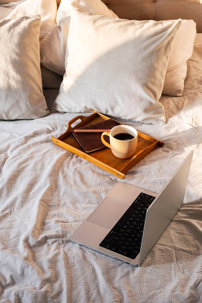 istock Open laptop and coffee cup bathed in morning sunlight on bed. Concept of remote work comfort and inspiration. 2197568743