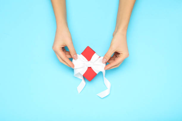istock Gift box with ribbon in female hands on blue background 2197569556