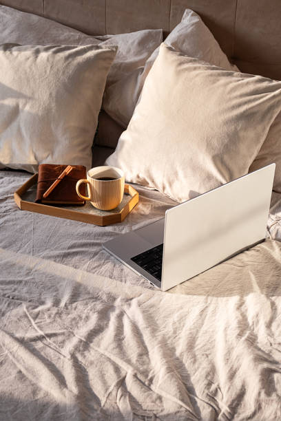 istock Sunlit morning workspace: open laptop and coffee cup on cozy bed. Remote work inspiration. 2197574461
