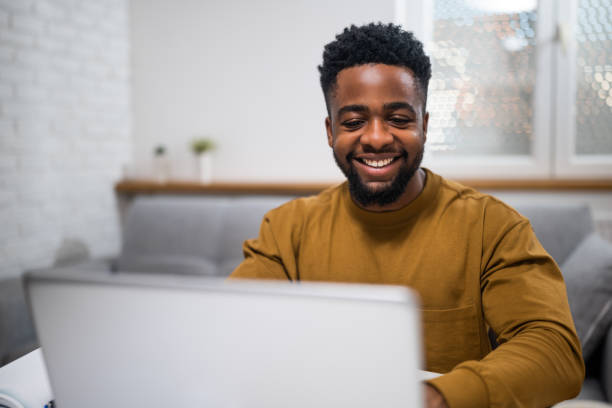 istock Young black man freelancer smiling and typing on laptop in home office 2197575407
