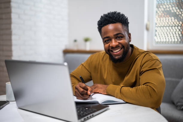istock Cheerful black businessman writing notes and using laptop at home office 2197575489