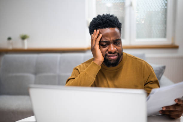 istock Overworked young black man looking at documents and using laptop at home 2197575564