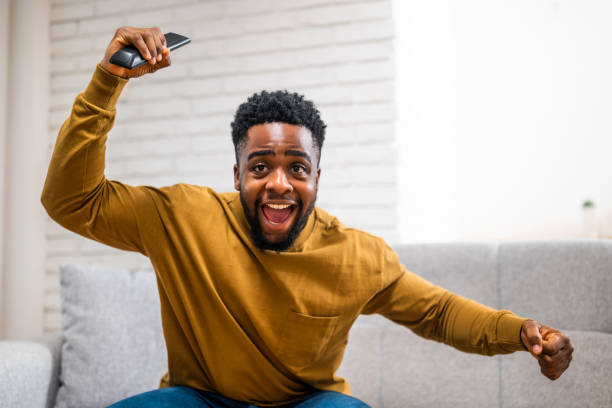 istock Happy black man cheering while watching sport game on tv 2197575582