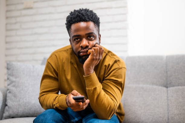istock Disappointed man holding remote control and changing channels on tv at home 2197575584