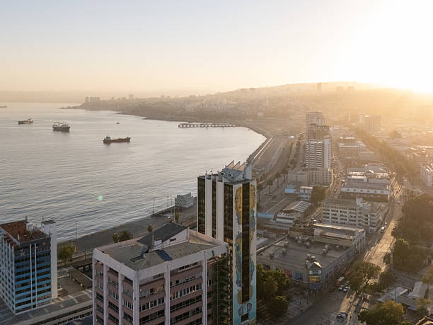 Sunrise over the bustling cityscape with a view of the coastal line. Aerial perspective highlighting urban architecture. Tranquil morning scene with warm sunlight.