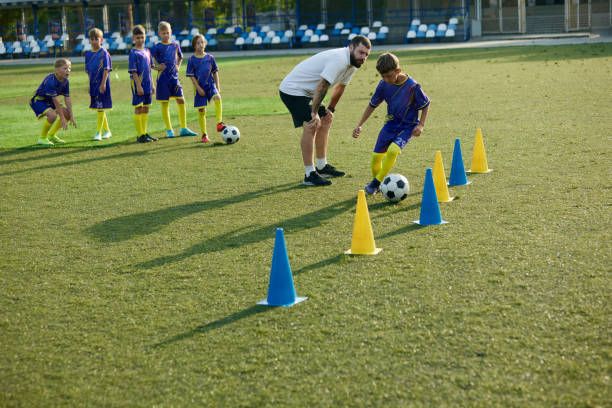 istock Boy, child, soccer player navigating ball through cones, while coach providing instruction and support. Outdoor football game 2197579009